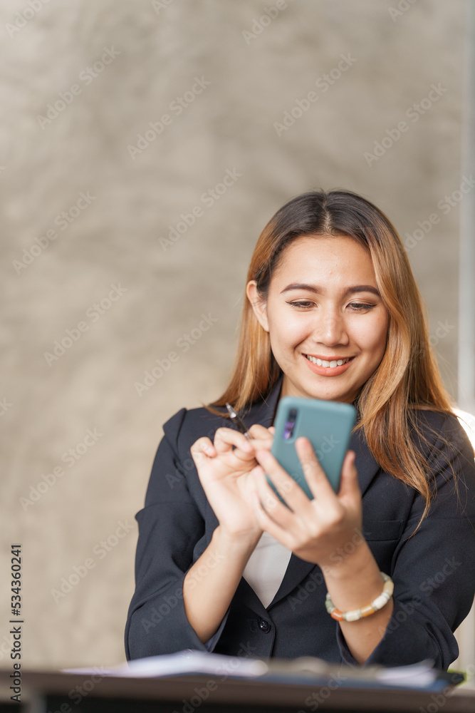 Young pretty asian stock manager checking list of product and working at workstation, using mobile phone. Young pretty asian stock manager checking list of product and working at workstation, using mobile phone.