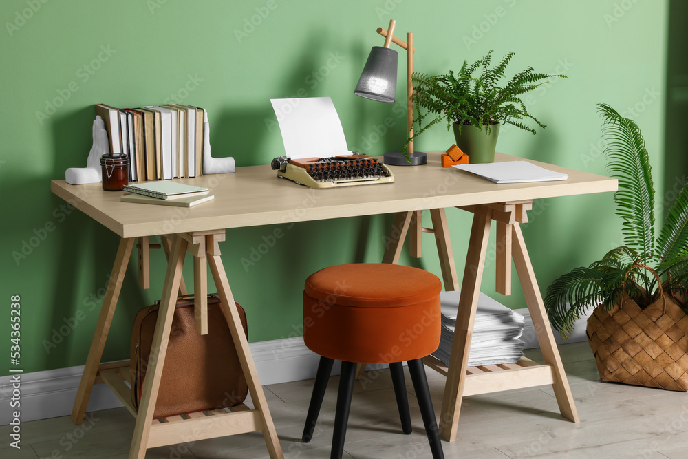Fototapeta premium Writer's workplace with typewriter on wooden desk near pale green wall in room