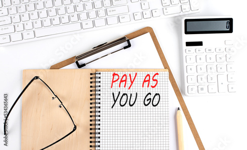 Notebook with the word PAY AS YOU GO with keyboard and calculator on the white background photo