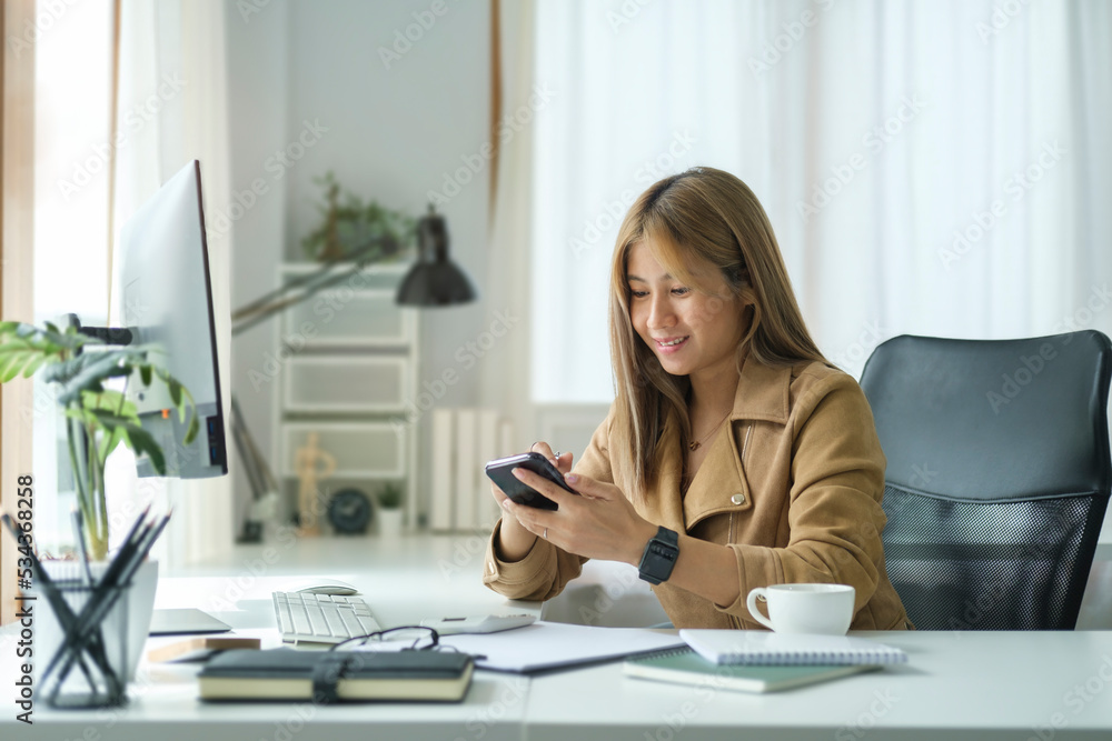 Smiling young businesswoman sitting at her office desk and using smart phone. Smiling young businesswoman sitting at her office desk and using smart phone.