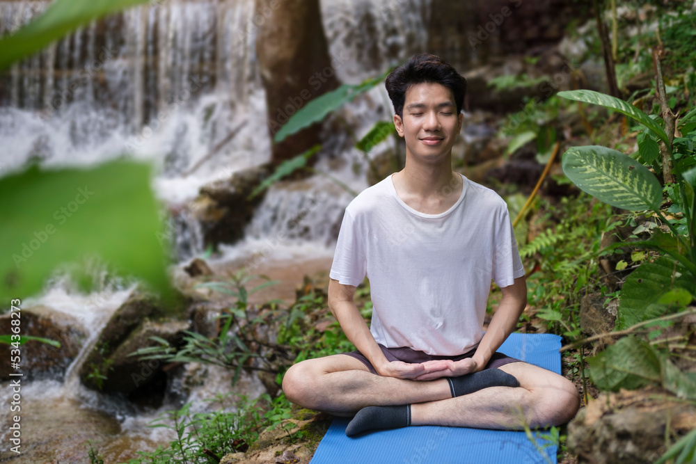 Man meditating, sitting on the rocks near the waterfall in the rain forest. Sport, yoga, pilates, fitness, healthy lifestyle concept. Man meditating, sitting on the rocks near the waterfall in the rain forest. Sport, yoga, pilates, fitness, healthy lifestyle concept.