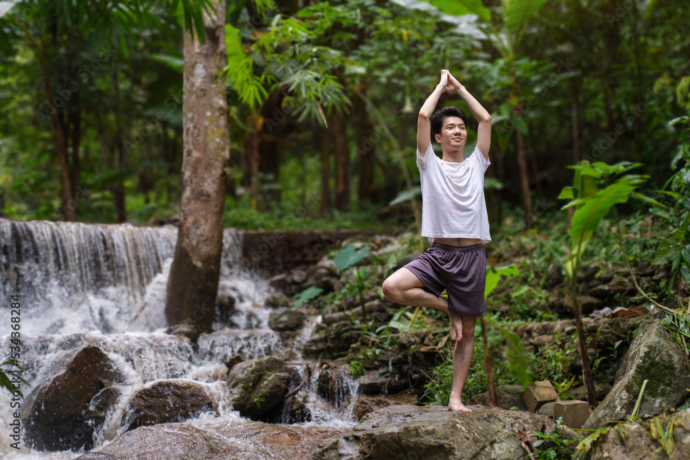 Healthy man practicing yoga on rocks near waterfall in the forest. Concept of calm and meditation. Healthy man practicing yoga on rocks near waterfall in the forest. Concept of calm and meditation.