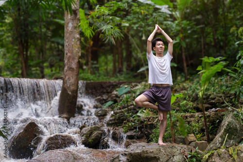 Healthy man practicing yoga on  rocks near waterfall in the forest. Concept of calm and meditation.