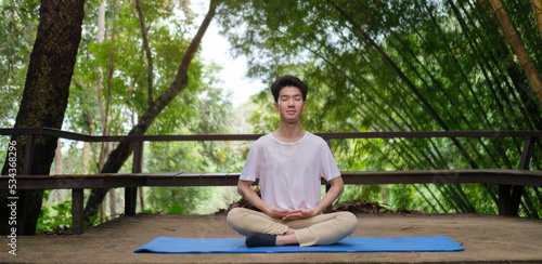 Young man practicing yoga and meditating at open yoga studio with beautiful nature view in background.