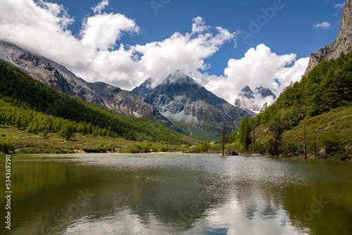 The mountain covered by cloud and a calm river in Daocheng Yading, Sichuan, China, horizontal image with copy space for text © Tatiana Kashko