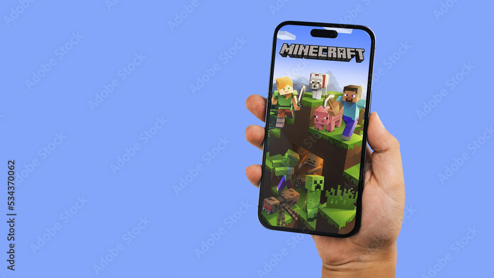 Fototapeta premium Child holding a smartphone iPhone 14 Pro with Minecraft mobile game app on the screen. Blue background. Rio de Janeiro, RJ, Brazil. September 2022