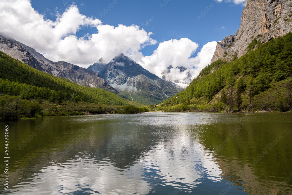 Yangmaiyong mountain range and turquoise river with mountain reflection surrounded with yellow pine forest in clear blue sky day in autumn season at Yading National Park, Daocheng, Sichuan, China