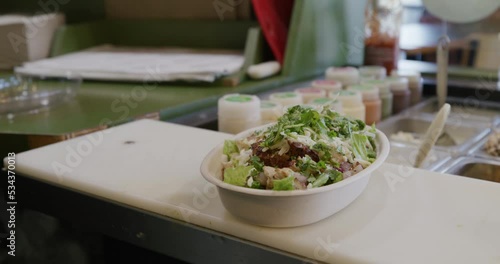 Closeup shot of server packing a freshly made salad bowl behind a restaurant counter.