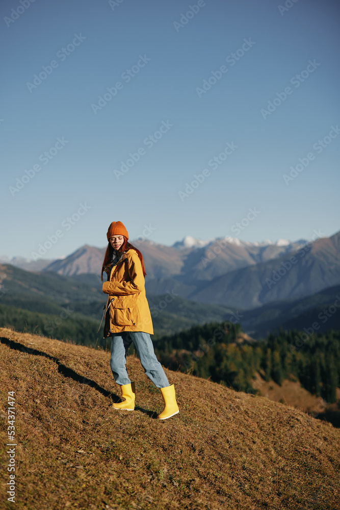 Woman walking full-length on a hill in the fall and looking out over the mountains in a yellow raincoat and jeans happy camping trip, freedom lifestyle 