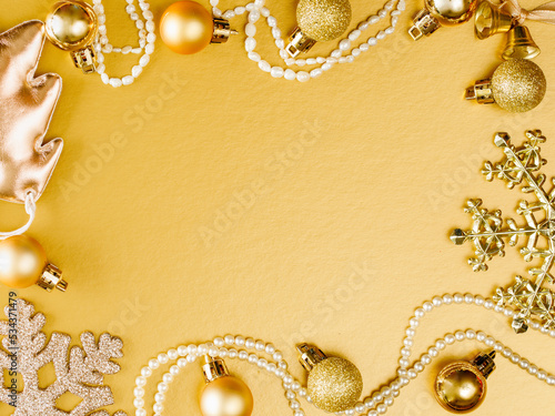 New Year and Christmas composition. Frame from yellow balls, glitter snowflake, beads, chrismas tree on pastel golden paper background. Top view, flat lay, copy space. Monochrome