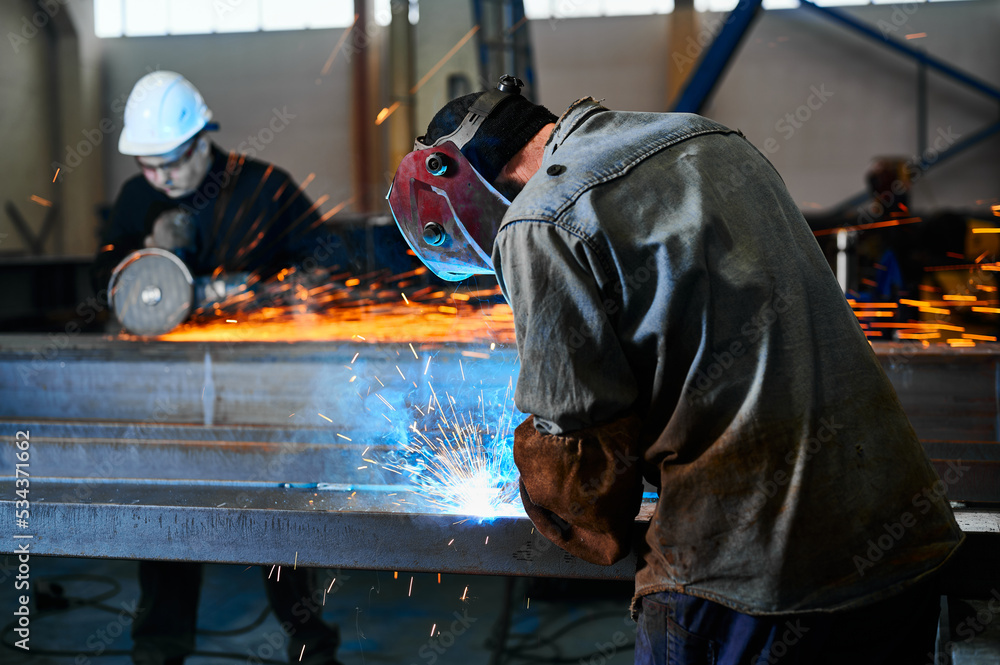 Worker with mask welds metal carcass parts in workshop Worker with mask welds metal carcass parts in workshop