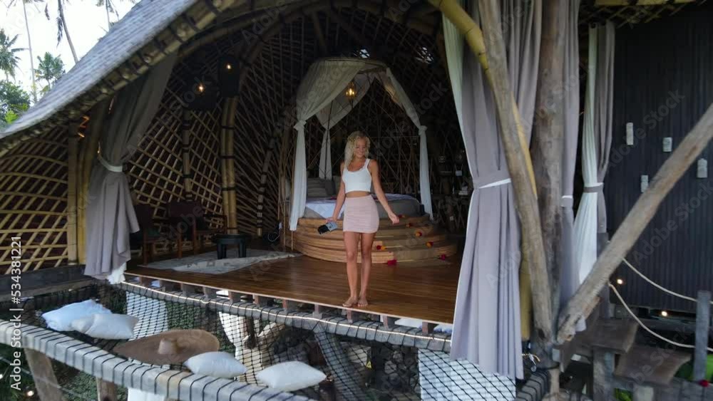 Drone shot of a sexy blond girl walking next to a bed in a bamboo house in Bali and her boyfriend dancing on the other floor. Romantic honeymoon. Drone shot of a sexy blond girl walking next to a bed in a bamboo house in Bali and her boyfriend dancing on the other floor. Romantic honeymoon.