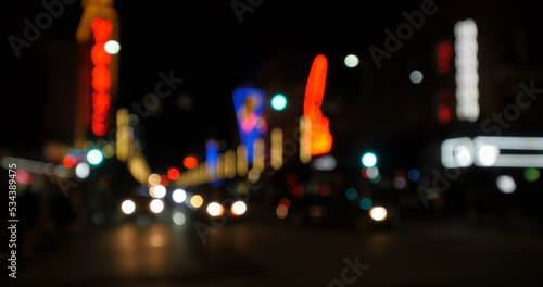 Image of defocussed shopfront lights with street lighting and traffic on a city road at night © vectorfusionart