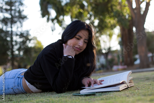 Young woman lying in a park reading a book. Concept of people and lifestyles.