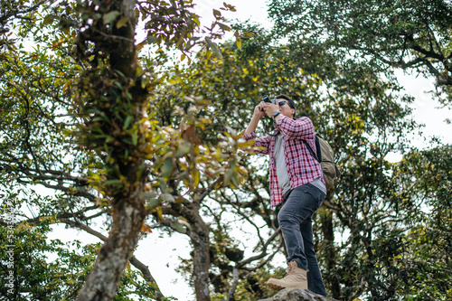 Young backpacker man use camera to take pictures in forest.