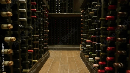 Slow motion pushing through rows of wine in dark home wine cellar