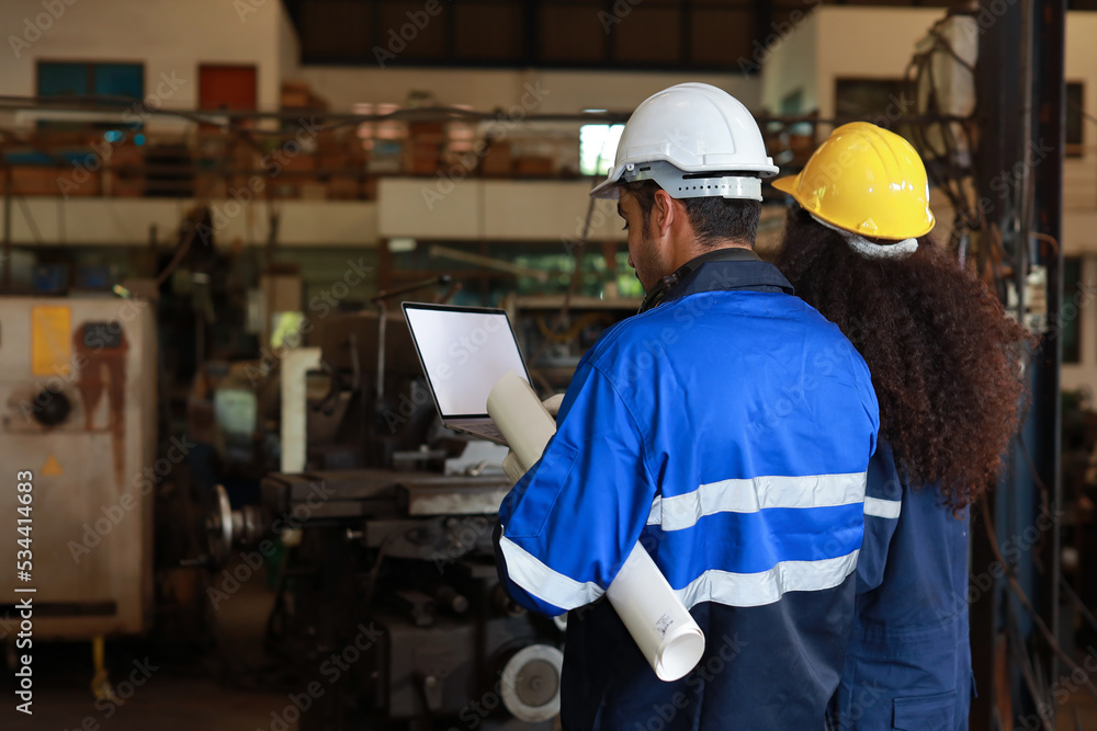 Rear view architect or worker checking at heavy industry manufacturing factory with walkie talkie radio and blueprint. Multiethnic business manager looking in future with warehouse factory building Rear view architect or worker checking at heavy industry manufacturing factory with walkie talkie radio and blueprint. Multiethnic business manager looking in future with warehouse factory building