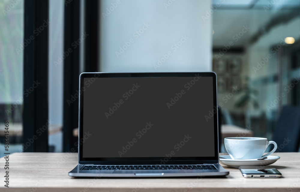Mockup of laptop computer with empty screen with coffee cup and smartphone on table of the coffee shop background,ฺ Black gray screen