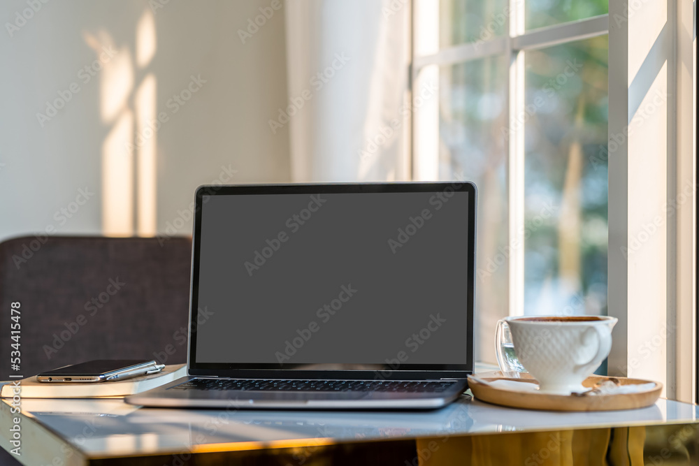 Mockup of laptop computer with empty screen with coffee cup and smartphone on table beside the window of the coffee shop background,Black gray screen