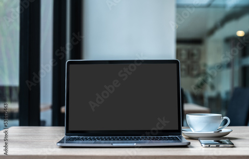 Obraz na płótnie Mockup of laptop computer with empty screen with coffee cup and smartphone on table of the coffee shop background,ฺ Black gray screen w salonie