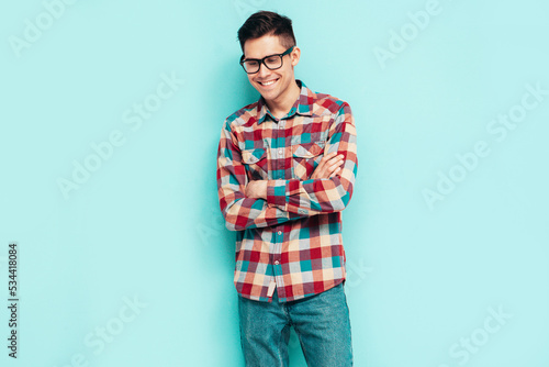 Portrait of handsome smiling model. Sexy stylish man dressed in checkered shirt and jeans. Fashion hipster male posing near blue wall in studio. Isolated. In glasses, spectacles