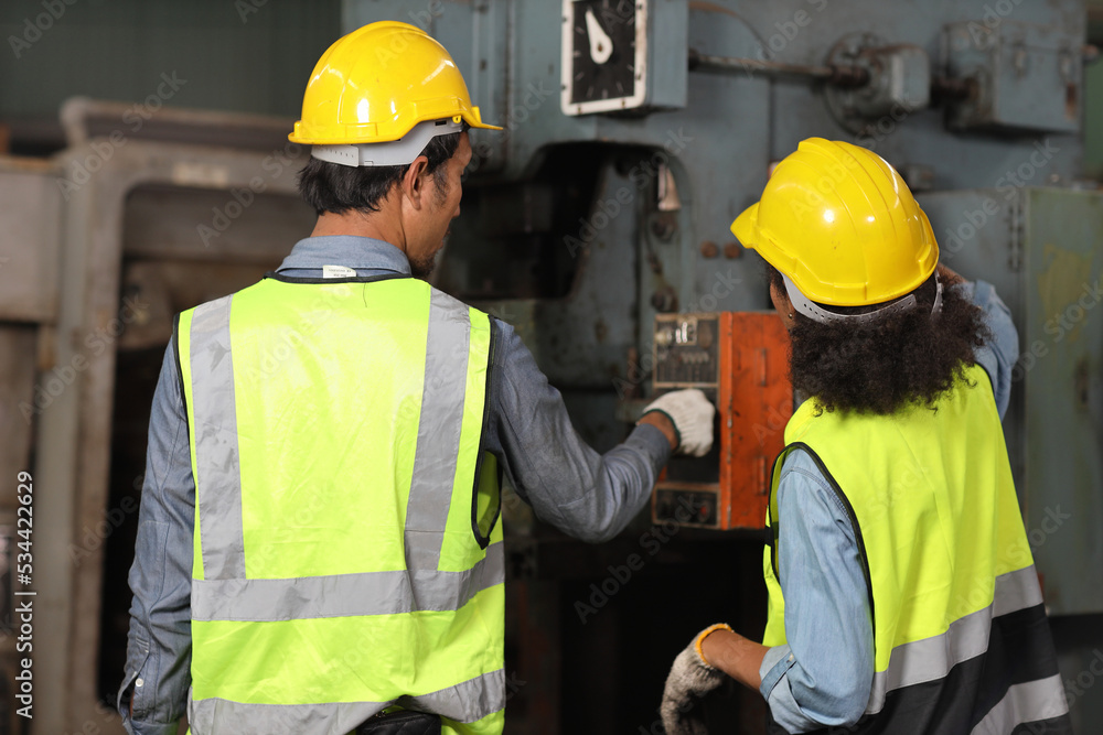 Rear view technician engineer or worker man and woman in protective suit standing and repairing operation or check industry machine process with safety hardhat at heavy industry manufacturing factory