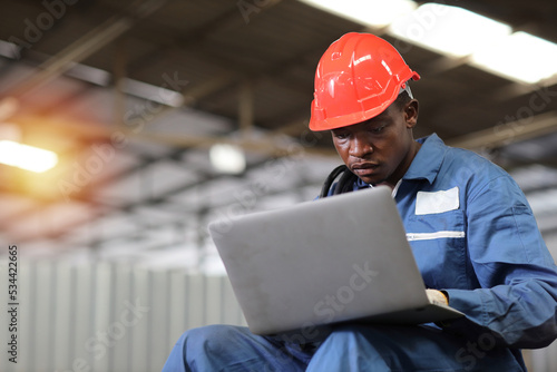 Engineer or worker man in protective uniform sitting and using computer while pose thinking something and controlling work with hardhat and electric cable line at heavy industry manufacturing factory