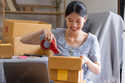 Young Asian woman small business owner SME online marketing at home. confirm orders from customers preparing package product with box and lapptop, SME entrepreneur or freelance life style concept.