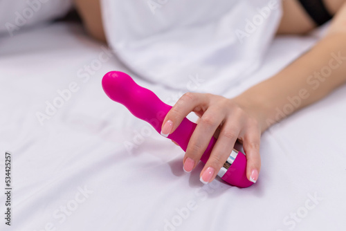 Woman in bed under sheets holding vibrator in hand photo