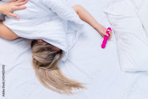 Woman in bed under sheets holding vibrator in hand photo