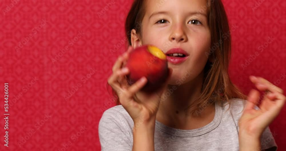 Portrait happy girl eats a peach on a red background, bites a juicy peach. The concept of enjoyment Portrait happy girl eats a peach on a red background, bites a juicy peach. The concept of enjoyment