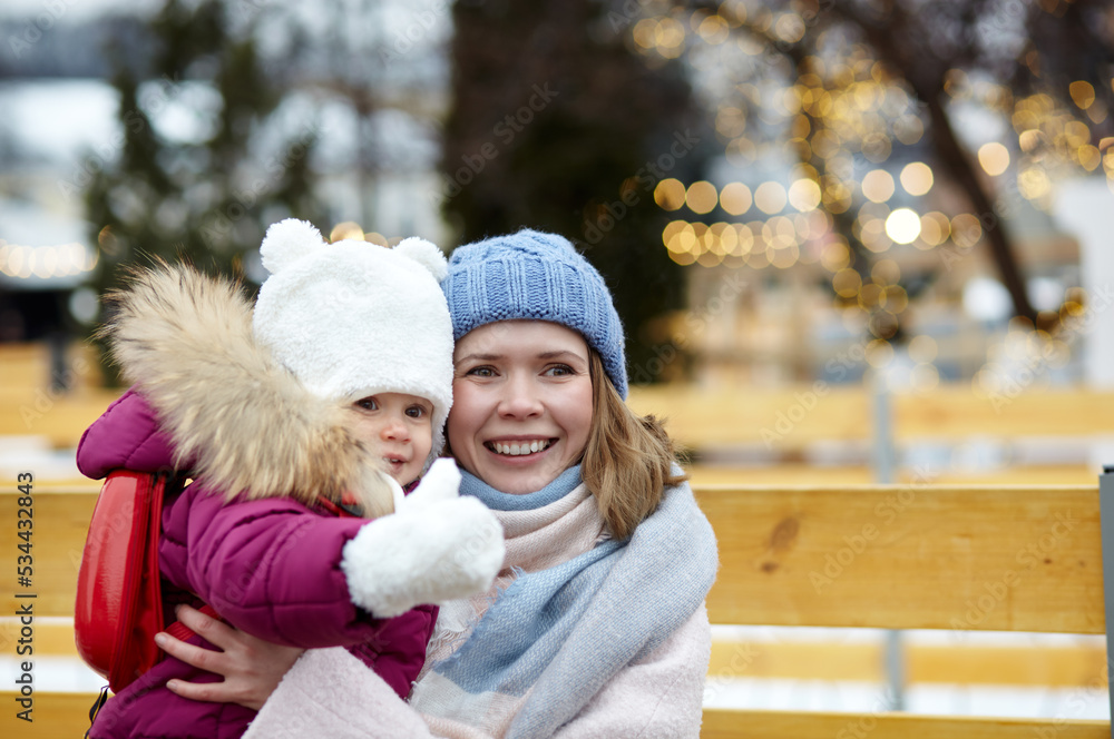 Fototapeta premium Mother and daughter are walking around the city on Christmas and New Year holidays. Parent and little child having fun outdoors