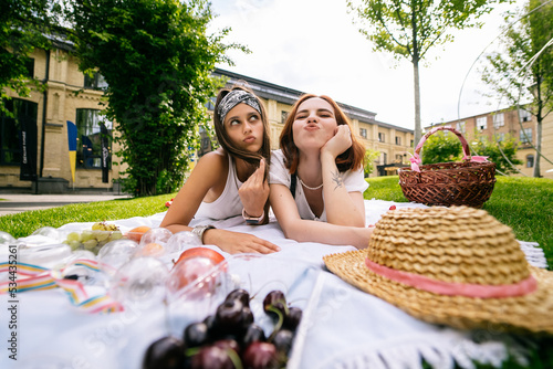 Two women having picnic together, laying on the park lawn