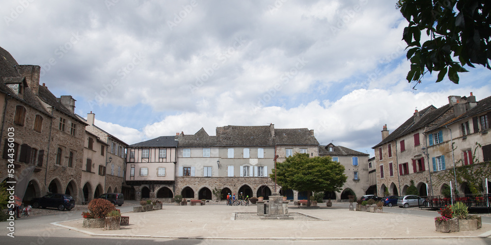 Fototapeta premium Cyclistes sur la place à arcades de Sauveterre de Rouergue dans le Lot