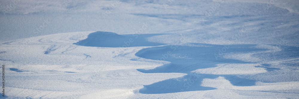 Snow texture. Wind sculpted patterns on snow surface. Wind in the tundra and in the mountains on the surface of the snow sculpts patterns and ridges. Arctic, Polar region. Winter panoramic background. Snow texture. Wind sculpted patterns on snow surface. Wind in the tundra and in the mountains on the surface of the snow sculpts patterns and ridges. Arctic, Polar region. Winter panoramic background.