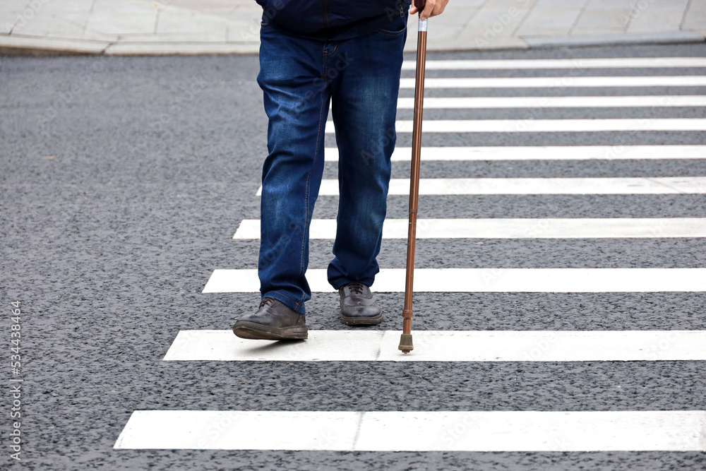 Man walking with a cane on crosswalk. Male legs on pedestrian crossing, street safety Man walking with a cane on crosswalk. Male legs on pedestrian crossing, street safety