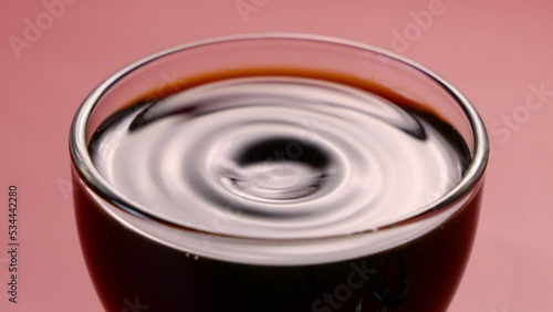 Coffee drop falling inside of transparent cup of espresso italian coffee on pink table. Drink and relax concept. Slow motion