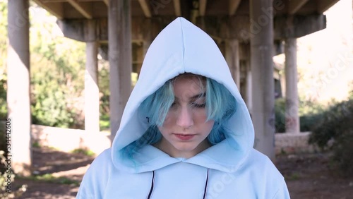 Teenager wearing blue oversize hoodie looking down. Blue haired teen girl staying outdoors against bridge pillars. Head shot. Hipster and adolescence concept