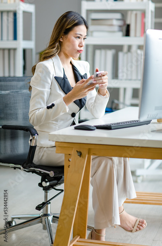 Asian female businesswoman search computer information while uesing mobile phone. Manager agent solve help to company customer distantly modern tech usage, busy fruitful workday concept photo