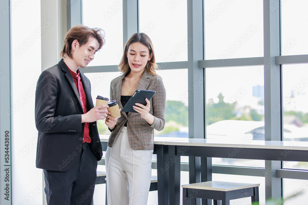 Millennial Asian successful professional female businesswoman in formal suit standing smiling showing data information on touchscreen tablet computer to male businessman colleague in company office Millennial Asian successful professional female businesswoman in formal suit standing smiling showing data information on touchscreen tablet computer to male businessman colleague in company office