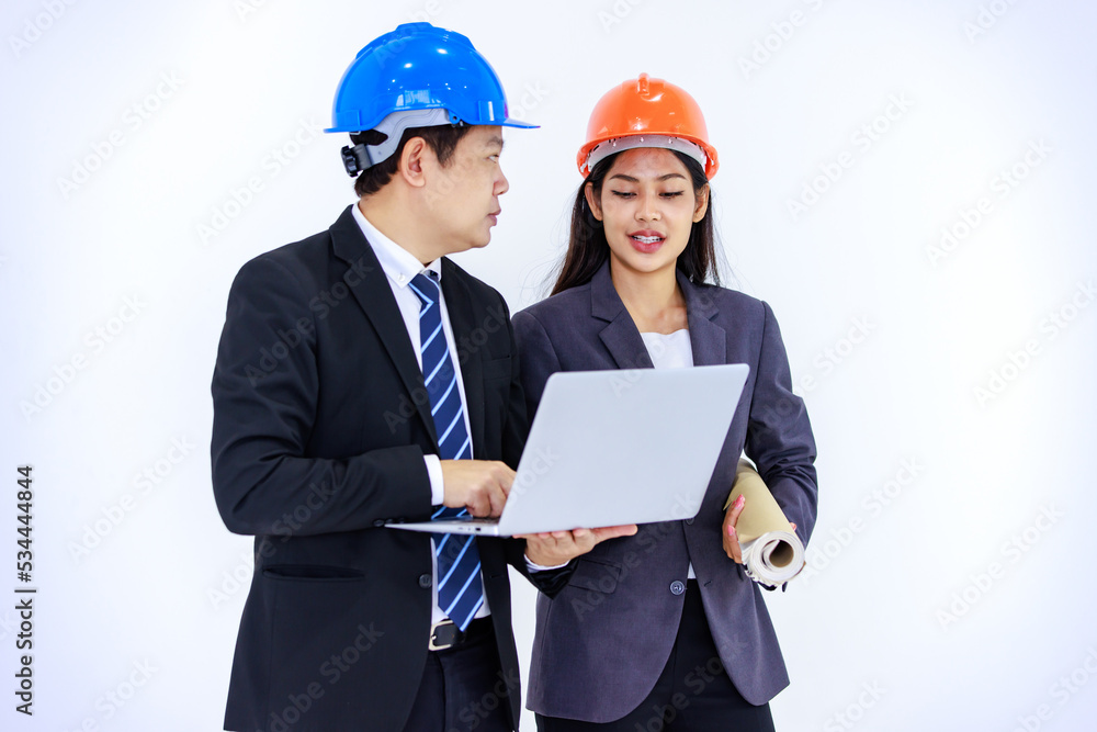 Millennial Asian successful professional male and female engineer in formal suit and safety hard helmet standing together holding blueprint looking at laptop notebook computer on white background Millennial Asian successful professional male and female engineer in formal suit and safety hard helmet standing together holding blueprint looking at laptop notebook computer on white background