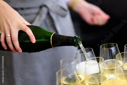 closeup of a champagne bottle pooring champagne into a champagne flute against a blurred person at a party