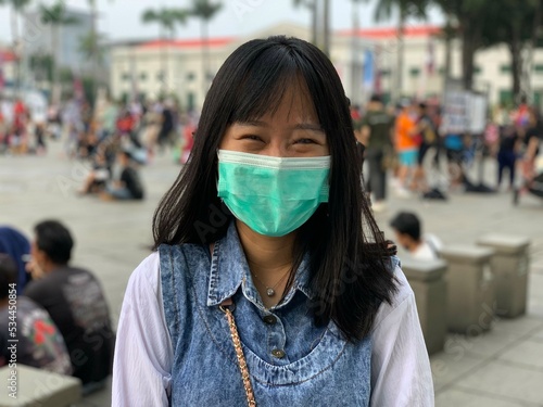 young asian woman with shoulder length hair wearing blue and white jeans and wearing a mask facing the camera in a public area. healthy concept. global pandemic