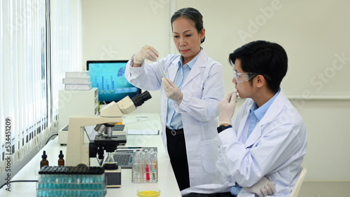 Two professional scientist conducting experiment with test tubes and microscope in research laboratory