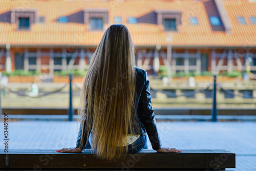 A long haired girl spending time alone in a city outdoors summer,autumn evening.Back view.Klaipeda,Lithuania.09-02-2022.