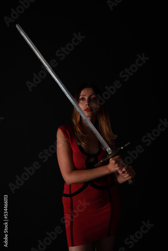 Woman in red dress holding sword in low key