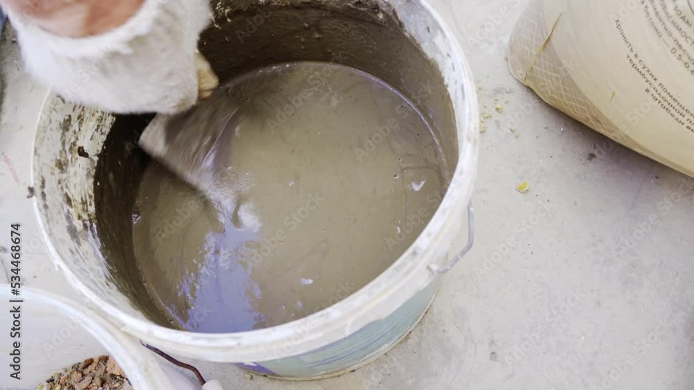 a gloved man's hand kneads cement mortar with a trowel. a gloved man's hand kneads cement mortar with a trowel.