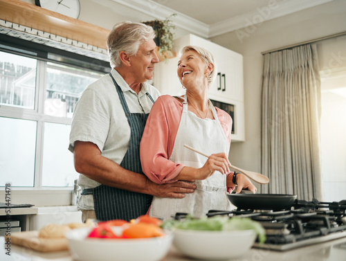 Senior couple, cooking and home bonding for fun, romance and happiness with husband hugging happy wife with love, care and offering help in the kitchen. Food, marriage and joy with old man and woman