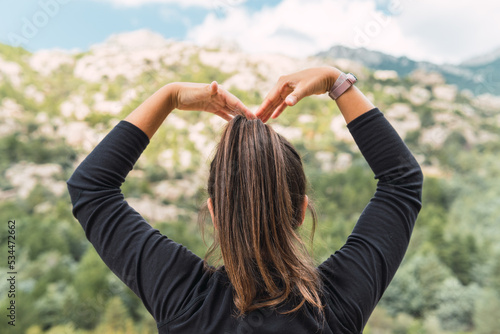 Unrecognizable young woman mountaineer in black sport shirt making with her arms the shape of a heart with the mountains in the background.