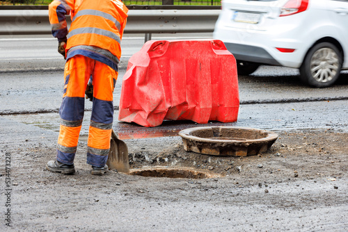 A road worker cleans the mouth of a sewer manhole on the roadway against the background of a passing car in blur. photo